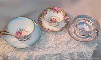 Top view of three floral patterned cups with matching saucers arranged on lace cloth, showing cup interiors and patterns.