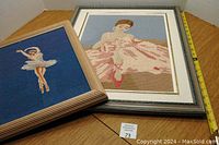 Two framed ballerina needlework pictures shown side by side with measuring tape for size reference