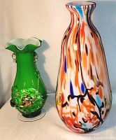 Photo showing green Tivoli vase with applied flower medallions and tall multicolor Murano vase with colorful swirls and clear base