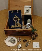 Open wooden jewelry box showing assorted costume jewelry including earrings, rings, brooches, and necklace with red stones and various metallic tones