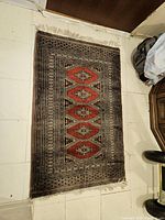 Full view of the rectangular gray and red area rug laid on a tiled floor showing the full pattern and condition.