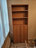 Front view of the pressed wood bookcase showing three open shelves above and two doors below with round knobs.