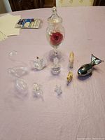 Overview of 9 small figurines and one glass jar with red rose inside on a padded surface.