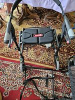 Two black walkers with seats and storage bags, placed on a patterned carpet