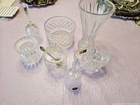 Overview of 6 crystal pieces on light pink tablecloth including vase, bowls, bells, covered and open dishes