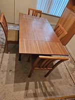 Dining table shown in partially extended position with four matching chairs around it, placed on carpet indoors.