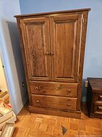 Wooden tall high boy cabinet showing overall front view with two doors and two drawers beneath.