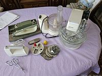 Four vintage kitchen appliances displayed on purple cloth including electric carving set and mixers.
