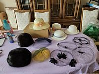 12 pieces total: 6 ladies hats and 6 fascinators displayed on a purple tablecloth including wide-brimmed hats, fur hats, and decorative netted fascinators