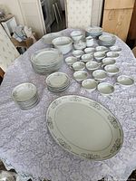 Full layout of Mikasa dinnerware set displayed on purple lace tablecloth including plates, cups, bowls, serving trays, and cream and sugar set.