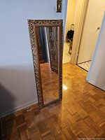Full view of the tall rectangular mirror showing the ornate carved wooden frame and reflective glass surface.