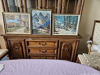 Three framed needlepoint landscape artworks on a wooden sideboard, showing size and style.
