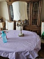 Full view of ornate table lamp with fabric shade and detailed base on table with purple cloth.