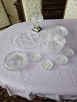 View of all crystal items arranged on a table including covered candy dish, footed bowls, ashtray, coasters and serving tray.