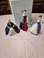 Set of three Royal Doulton figurines displayed on a table with original box in background