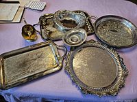 Silver plated trays, bowls, and sugar dish arranged on table showing details and condition.