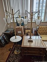 Two brass lamps shown side by side in room, floor lamp taller with three lantern glass shades with etched patterns and hanging crystal prisms, table lamp smaller with matching design.