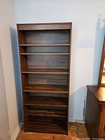 Front view of the shelving unit showing its full height and six shelves with dark brown wood grain finish.
