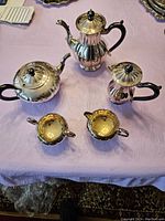 Full view of all five pieces laid out on a table, showing teapot, coffee pot, covered milk jug, sugar bowl, and creamer with wooden handles and finials