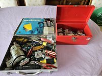 Overview of metal carrying case open showing various hand tools including screwdrivers, pliers, tape measures, and sandpaper pack.