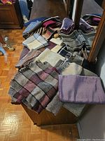 Large group of folded scarves on wooden furniture with a mirror reflecting some of the scarves.