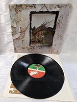 Photo of the front of the Led Zeppelin IV record sleeve and vinyl record on top of protective inner sleeve. Shows condition of sleeve with peeling and wear and good vinyl condition.