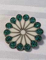 Front view of circular floral design pendant brooch with alternating white enamel and turquoise inlay petals.