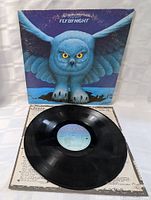Front view of the Fly By Night album sleeve with vinyl record partially leaning on it lying on a light surface.