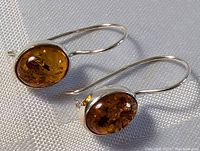 Close-up of the pair of sterling silver earrings with oval amber stones showing the translucent amber with natural inclusions and smooth silver hooks in good light.