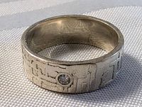 Close-up of chunky sterling silver ring with etched symbolic motif and small diamond on band