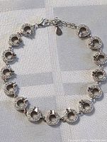 Sterling silver bracelet with circular horsebit-shaped encrusted links and lobster clasp laid out flat on fabric.