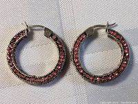 Front view of pair of sterling silver hoop earrings with pink rhinestones on a light fabric background.
