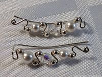 Close-up photo of the pair of sterling silver earrings lying on a white textured cloth, showing the abstract wavy design with pearl and crystal bead accents.