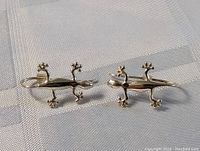 Pair of sterling silver gecko-shaped earrings displayed on fabric surface.