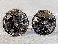 Photo showing full view of a pair of round sterling silver carved carved earrings with twist-on backs, detailed carving of floral and abstract shapes with polished finish.