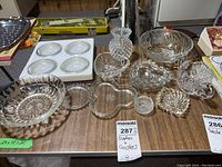 Photo showing a variety of clear glass dishes and coasters arranged on a table, showing different shapes and patterns including starburst, scalloped edges and hobnail textures.