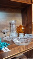 Shelf display showing all items: clear cut glass vase, amber glass bowl, divided serving dish, ashtray, butter dish, candle holders, and compote dish.