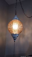 Full view of the amber glass swag lamp lit, showing globe and hanging chain.