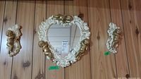 Heart-shaped mirror flanked by two cupid wall art pieces mounted on wood panel wall