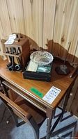 Wooden table with six smoking pipes in a wooden holder, glass ashtray, tissue box, and metal stand on a wooden side table against wood panel wall.