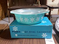 Front view of the Pyrex dish on its original box showing the snowflake pattern and glass lid.