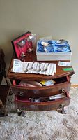 Photo of dresser top showing collector spoons laid out on cloth, two wine glasses, and dresser drawers partially open with flatware inside