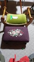Pair of vintage wood stools, one with green velvet upholstered seat and wood armrests, the other with floral embroidered purple cushion.