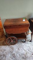 Front side view of the wood tea cart with one drop leaf down, showing the wood grain and decorative large wheels.