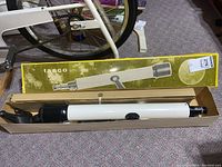 White Tasco telescope tube with black eyepiece and focusing knob inside original box on floor next to bike.