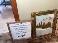 Two framed pieces of wall art standing against a wall, showing the quote and the mountain painting.