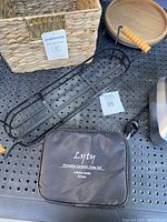 Photo of two woven baskets, portable ceramic sake set in black carrying case with brand Lyty, and black metal tiered display shelf with wooden handle on perforated surface.