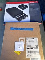 Photo showing two boxes: a Honeywell steel cash drawer box with product images and details, and a cardboard box labeled as an iPad stand for Square terminal.