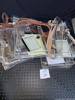 Photo showing several clear tote bags with brown leather strap handles, containing various small notebooks and notepads, all placed on a black perforated surface.