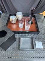Photo of tray with cups, glass tumblers, black vase, tissue box cover, and small tray on perforated surface